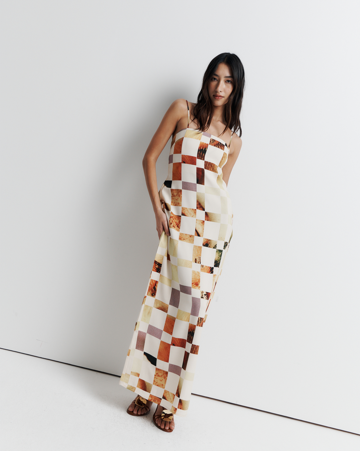 Model in a column dress with straight neckline, rouleau straps, invisible back zip, internal bustier with boning, checkerboard artwork by Phoebe Willis.