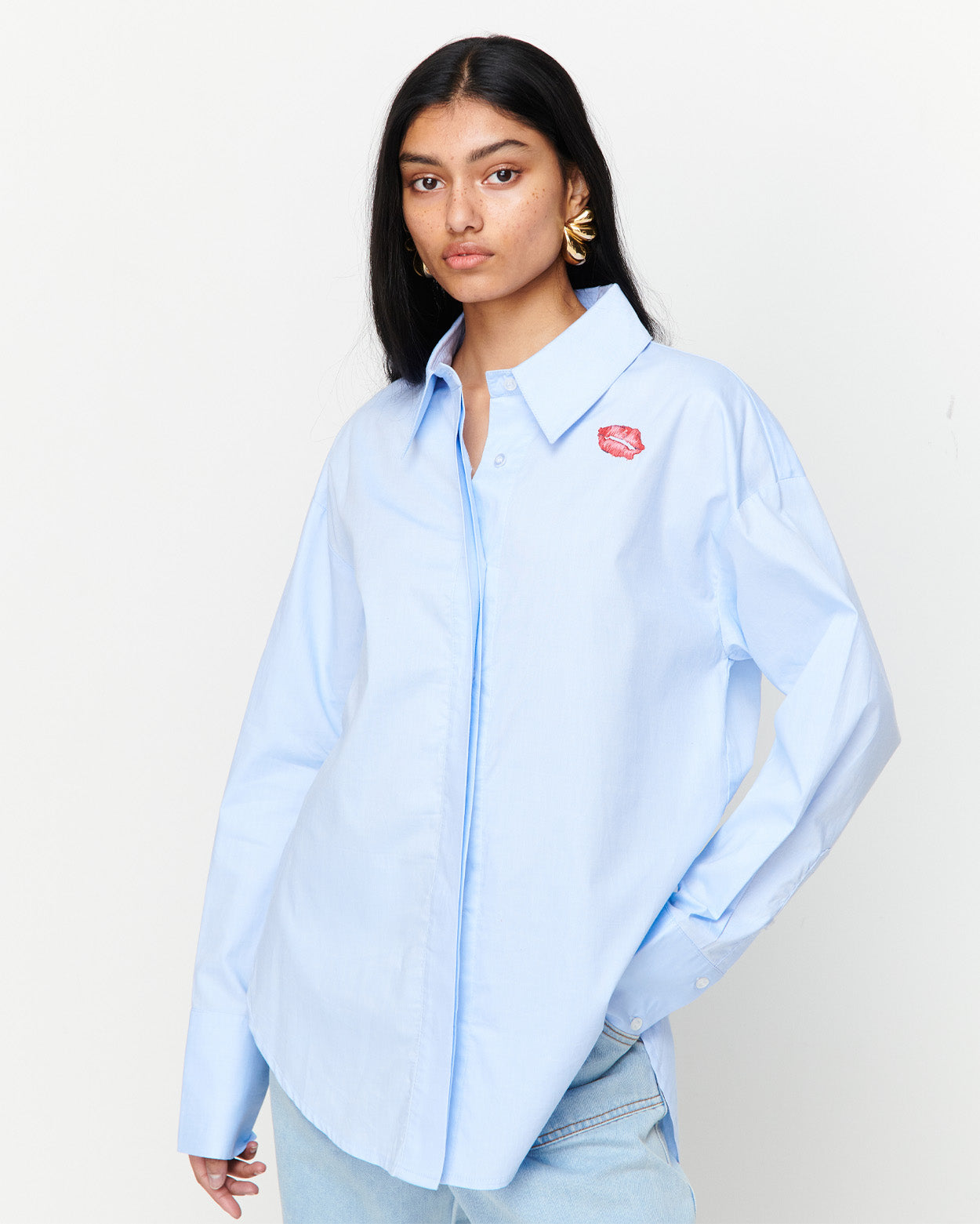 The Classic Cotton Shirt is an oversized essential, crafted from 100% cotton for effortless wear. Featuring a cheeky kiss embroidery under the left collar, this piece showcases exclusive artwork in collaboration with Anouk Colantoni.